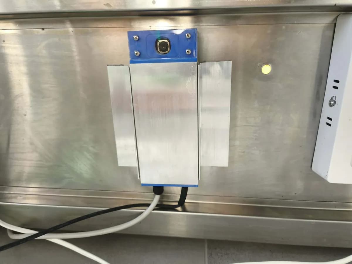The camera fixed to the underside of the stainless shelf with its cables