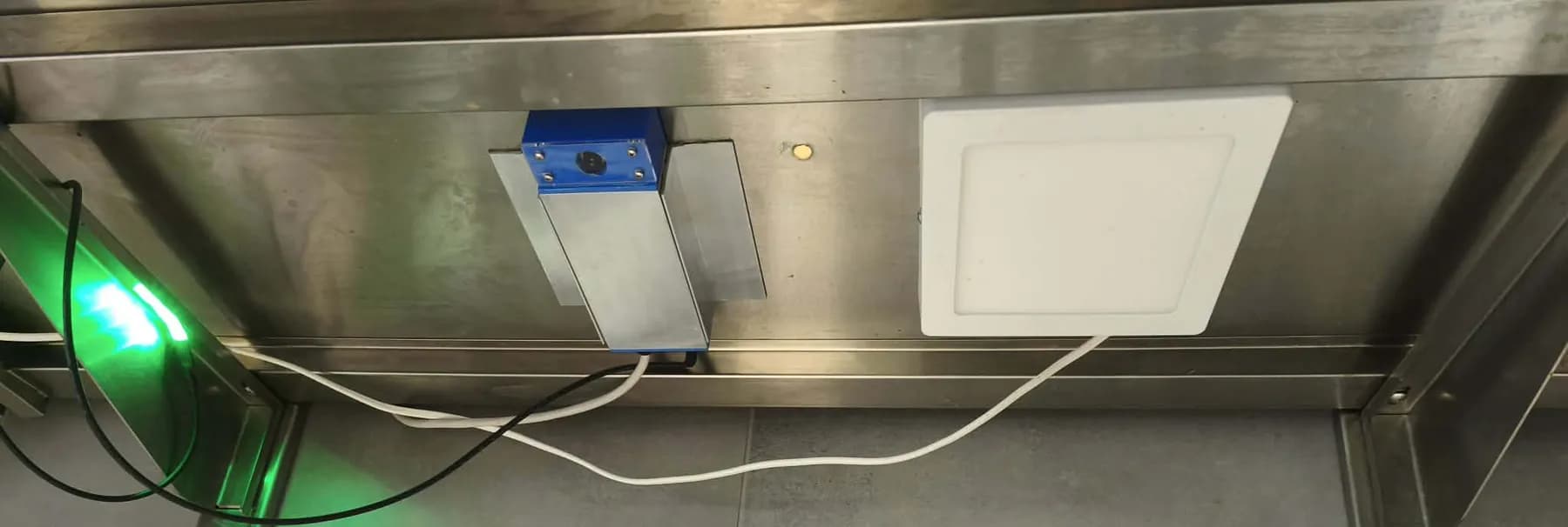 The underside of the shelf at the packing station with the camera, a square LED panel, and a green status light